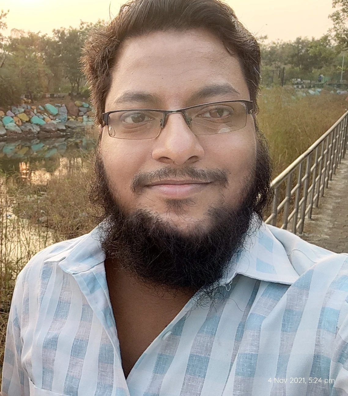 Mohammed Sharif smiling in a white plaid shirt and with glasses